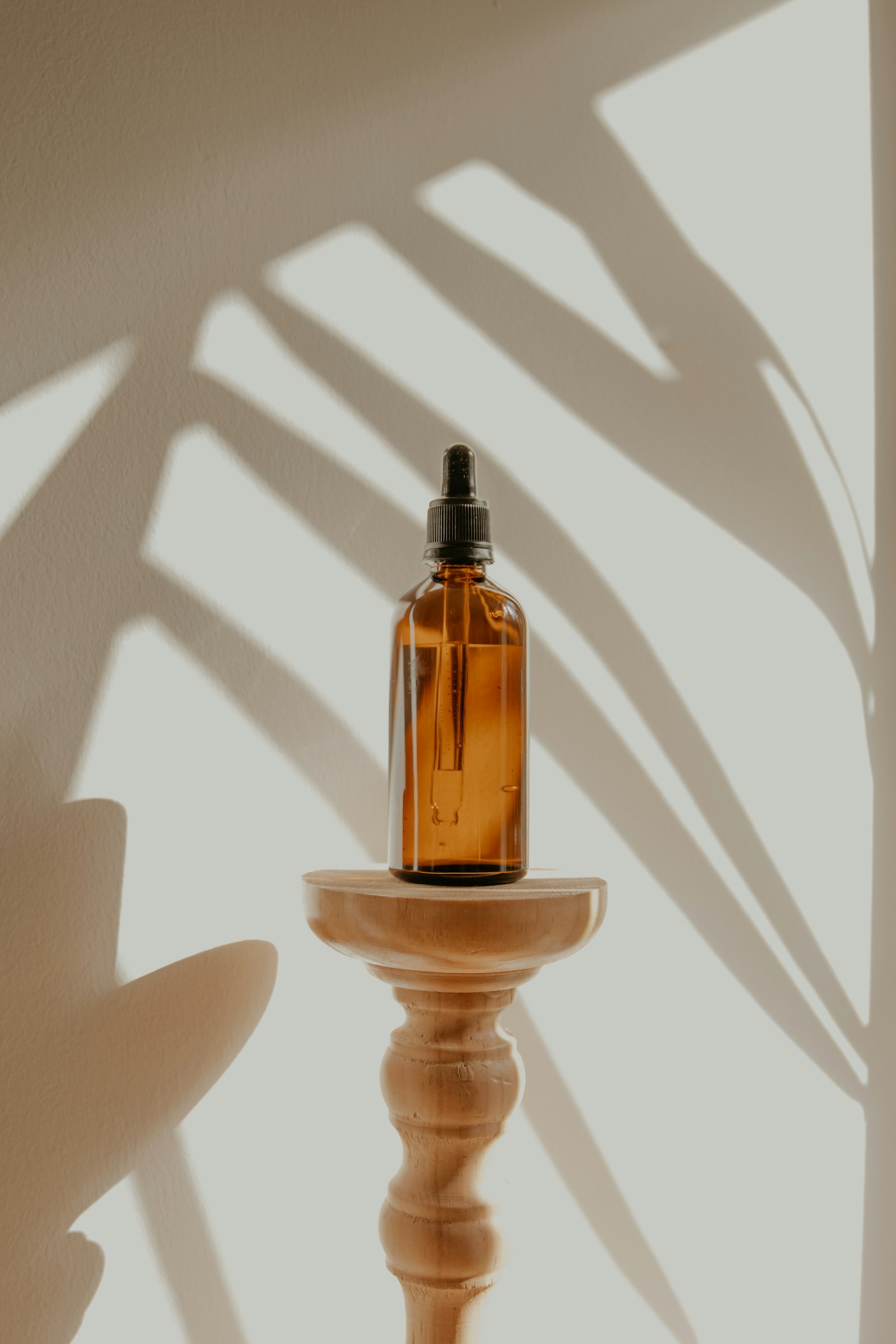 Amber glass dropper bottle on a wooden pedestal with soft leaf shadows